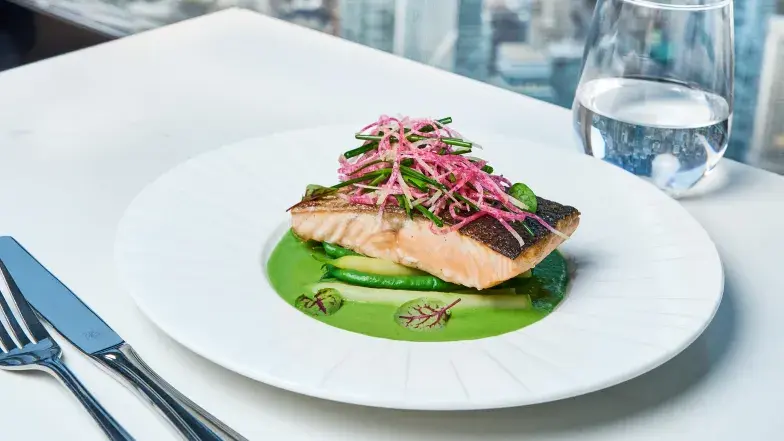 Seared salmon with green purée and pink garnish at 360 Restaurant, with cutlery and a water glass.