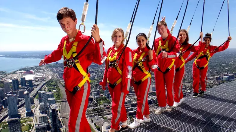 Group of seven people balancing on the edge of the walk. The city below them and clear skies behind them.
