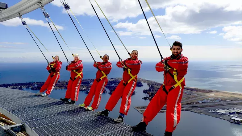 Group of five people with their backs leaning over the edge. Clouds and blue sky behind them.
