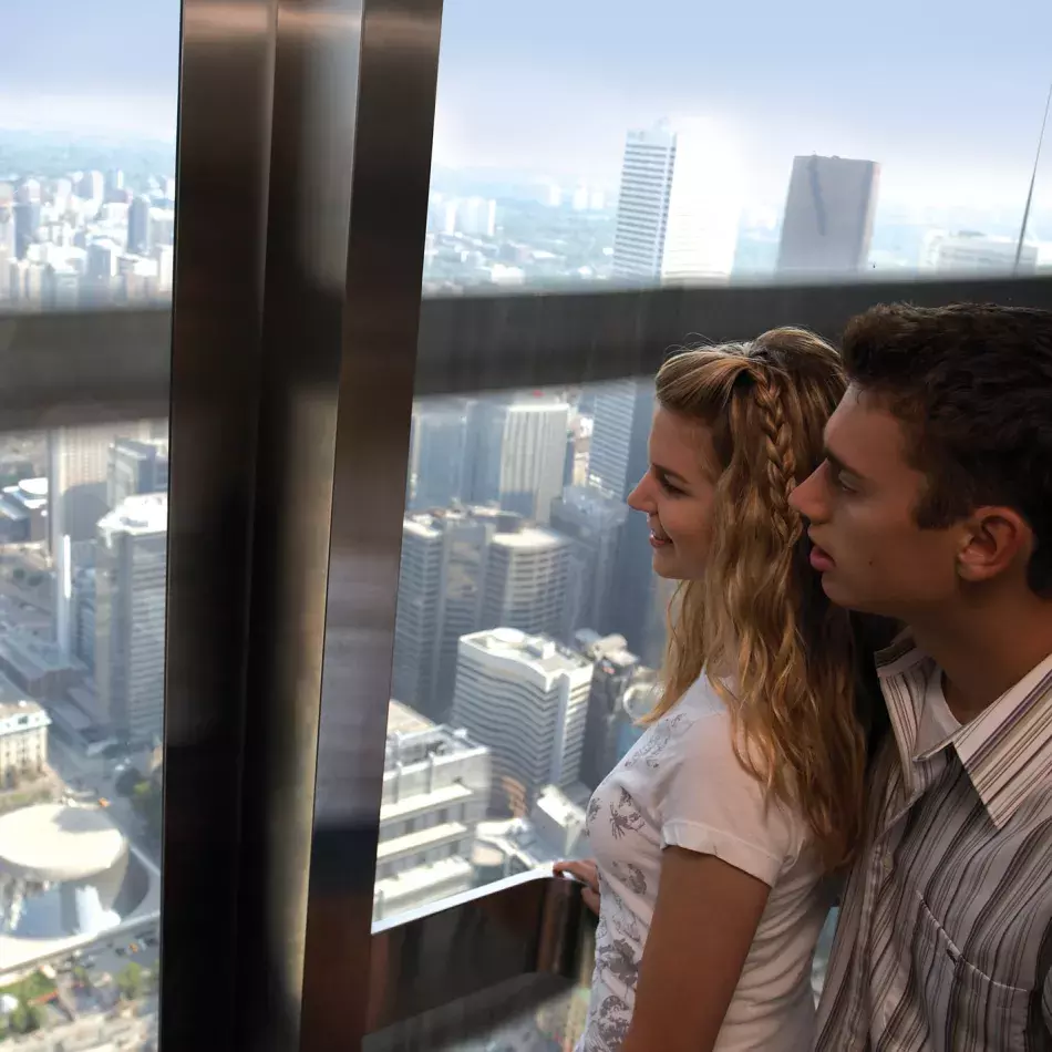Two people looking through the window of the elevator with the city in the background.